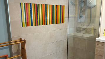 Een moderne badkamer met een douchecabine van glas, een houten handdoekrek en een kleurrijke wanddecoratie met strepen.