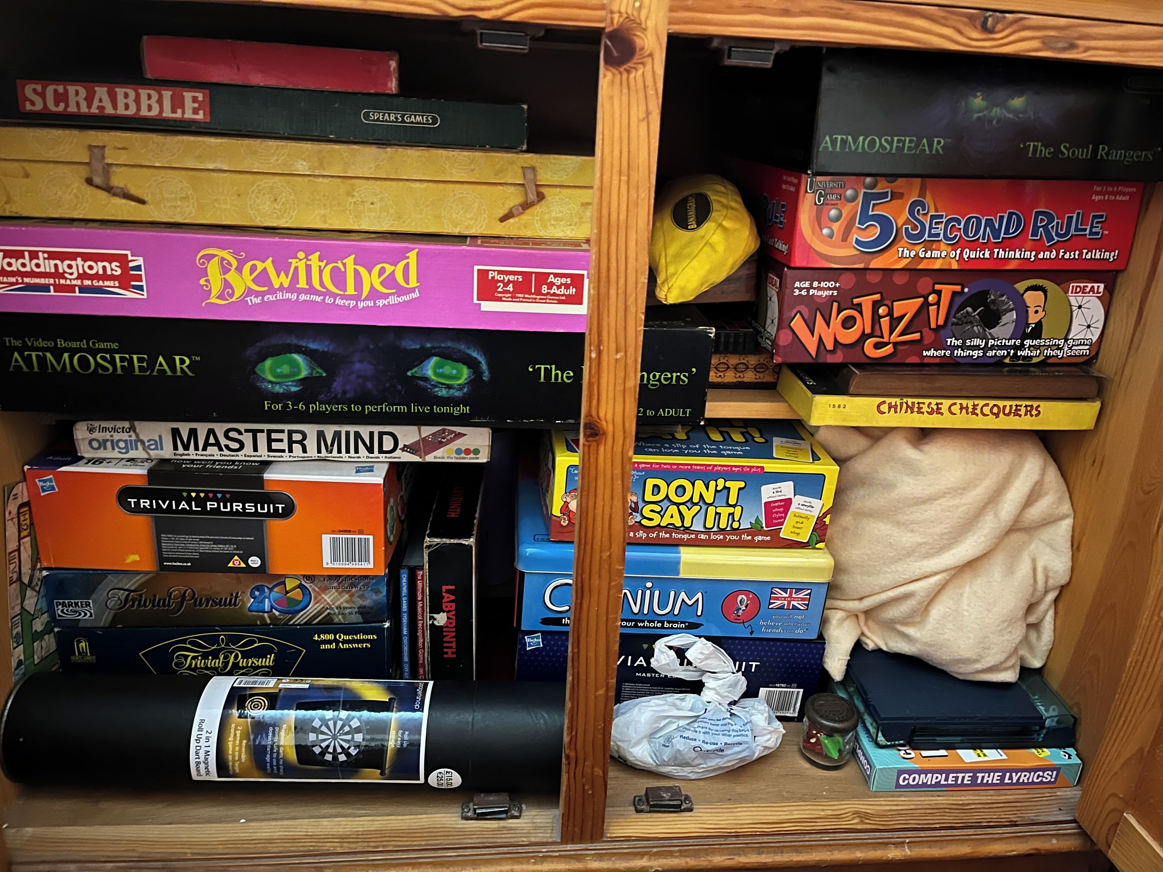 A wooden shelf with various board games and a dartboard.