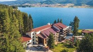 Un hôtel à plusieurs étages, doté d’un toit recouvert de tuiles rouges, entouré d’une végétation luxuriante et bordé d’un lac.
