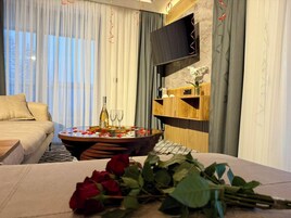 Una habitación de hotel moderna con una cama, una mesa redonda adornada con pétalos de rosa, una botella de vino y copas.