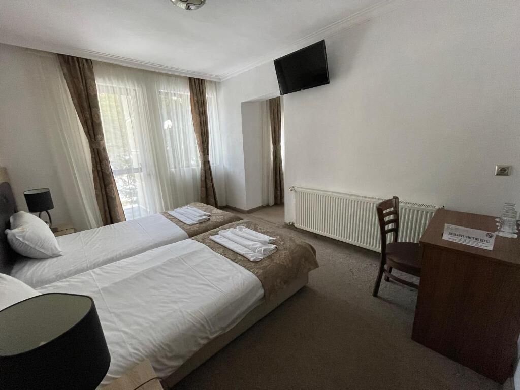 A hotel room with two beds, a desk, a chair, a television, and a radiator.