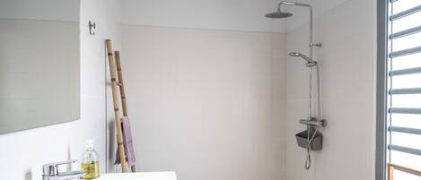Une salle de bain avec un lavabo blanc, un miroir, une douche et un sol carrelé.