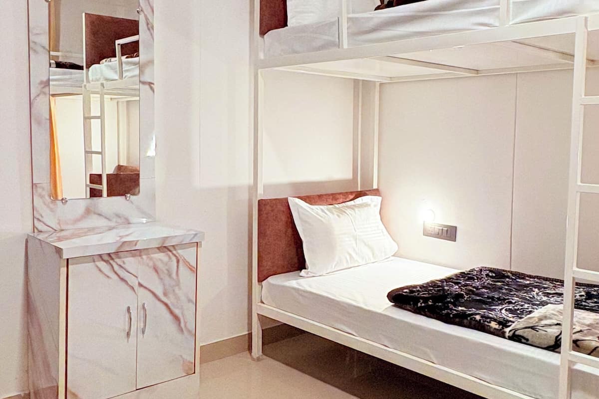A bunk bed with a mirror and a cabinet in a room with white walls and a tiled floor.