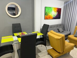 A modern living room with a glass table, black and yellow chairs, a gray sofa, and a colorful abstract painting on the wall. - AMOBLADO LOS MOLINOS (Medellín)