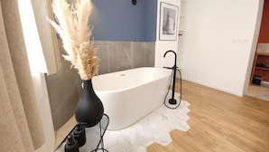 A modern bathroom with a freestanding bathtub, a vase with pampas grass, and a wall-mounted light fixture.
