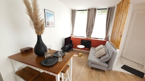 A modern living room with a dining table set for two, a grey sofa, and a fireplace.