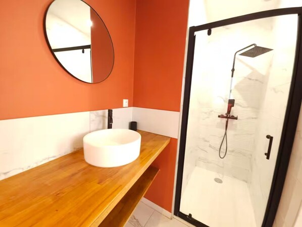 Un baño con tocador de madera, un espejo redondo y cabina de ducha con mampara de vidrio.