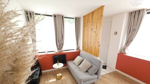 A modern living room with a grey sofa, wooden flooring, and a large window with curtains.