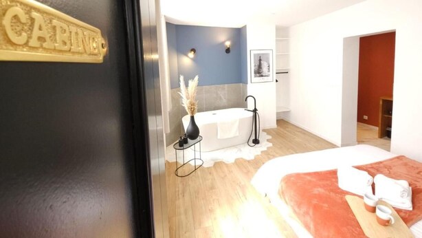 A hotel room with a bed, a bathroom with a bathtub, and a small table with a vase.
