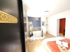 Una habitación de hotel con cama, baño con bañera y una pequeña mesa con un florero.