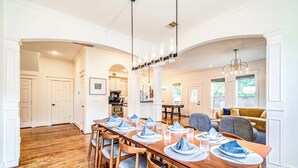 Un coin repas avec une table en bois dressée pour quatre personnes, flanquée de deux fauteuils gris, et une cuisine en arrière-plan.
