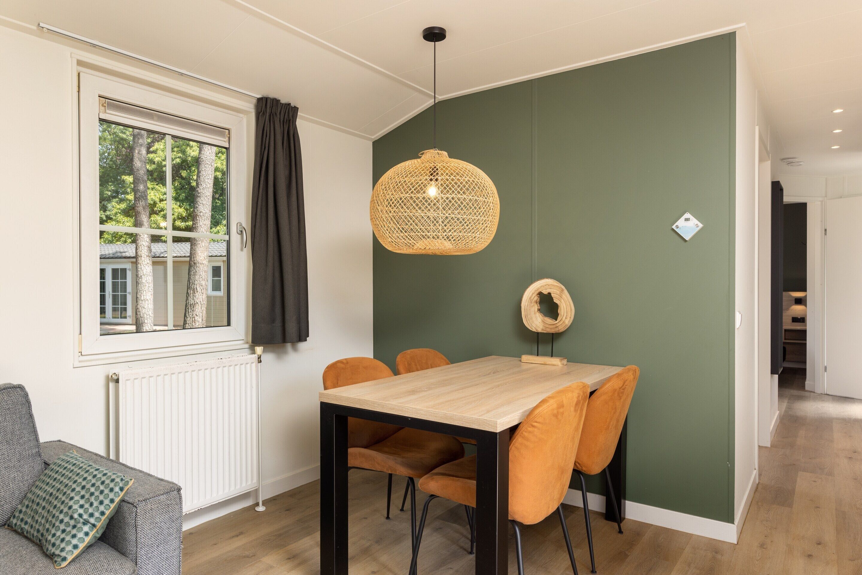 A dining area with a table and chairs, a hanging light fixture, a window with curtains, and a radiator.