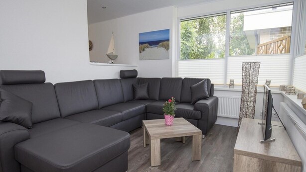 Una sala de estar moderna con un amplio sofá modular en forma de L, una mesa de centro de madera y un televisor sobre un mueble.