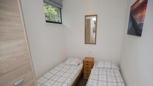 Un alojamiento pequeño y de una sola habitación con dos camas individuales, un armario de madera, un ventanal y un espejo en la pared.
