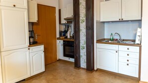 Cocina con armarios blancos, puerta de madera, pared de ladrillo decorativa y un lavamanos con una cesta sobre la encimera.