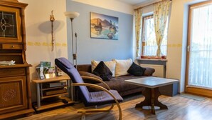 Una sala de estar con un sofá marrón, un sillón mecedora púrpura, un aparador de madera, una mesa y un cuadro en la pared.