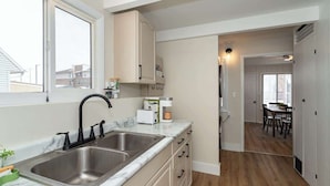 A modern kitchen with a double sink, white cabinets, and a view to a dining area. - 3BR Getaway, Sleeps 6 | 2-3 Miles to ISU (Ames)