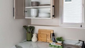 A compact kitchen with a marble countertop, a built-in cabinet with dishes, a sink, and a window with blinds. - 3BR Getaway, Sleeps 6 | 2-3 Miles to ISU (Ames)