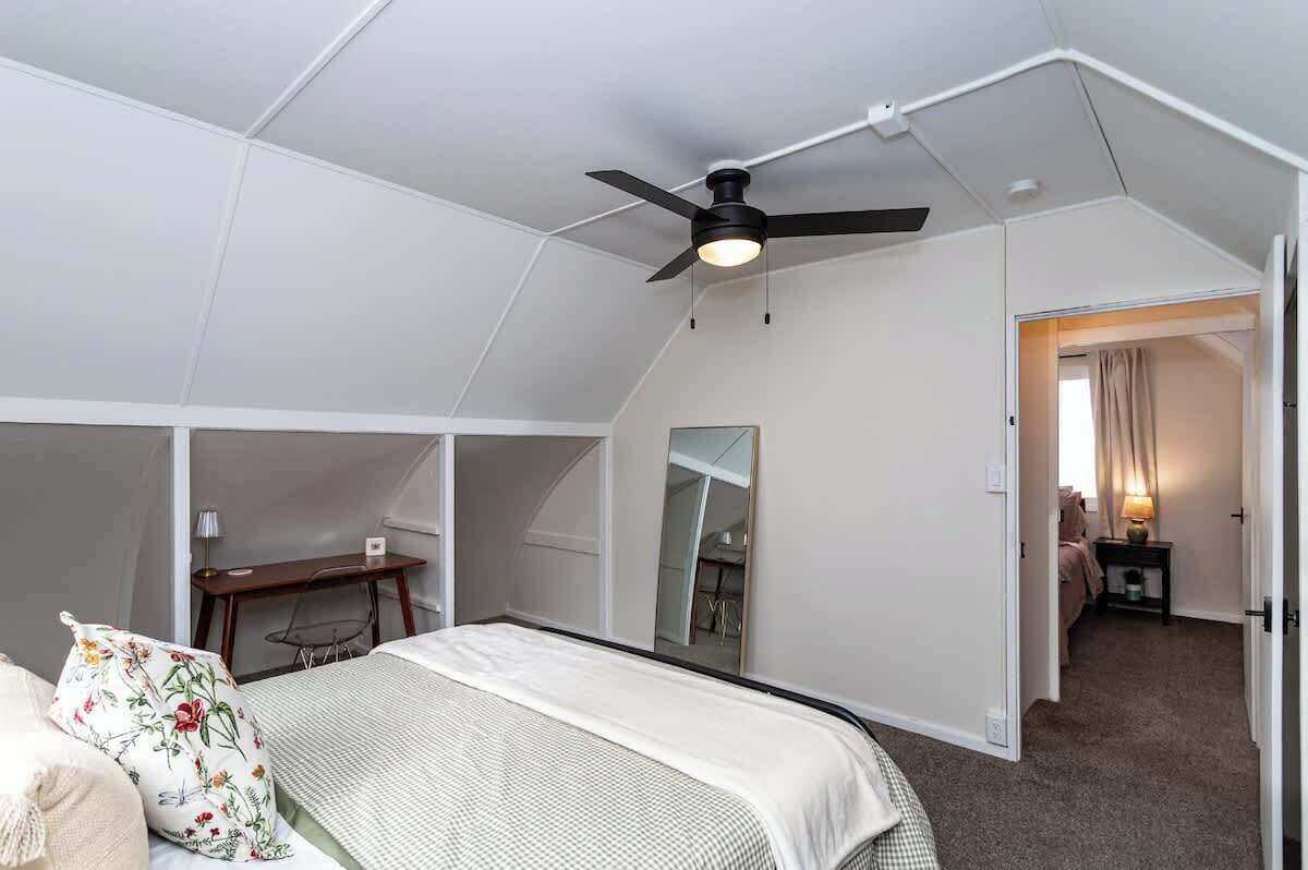 Ein Schlafzimmer mit Bett, Schreibtisch, Stuhl, Deckenventilator und Spiegel.