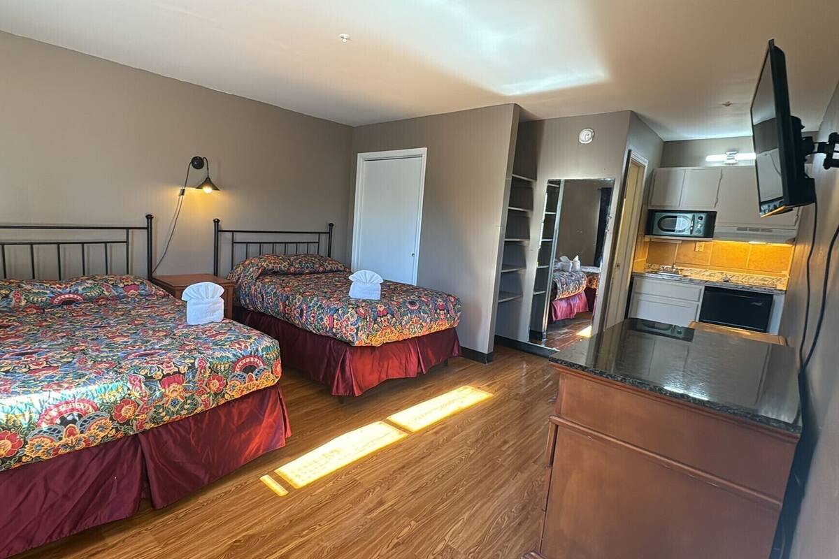 A compact room with two beds, a kitchenette, and a mirror.