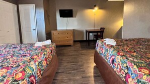 A room with two beds, a dresser, a desk, a chair, and a TV mounted on the wall. - Live In Lodge (Marietta)