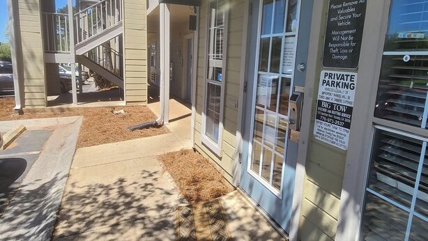 A building with a covered entrance, a staircase, and a sign indicating private parking with a towing policy. - Live In Lodge (Marietta)