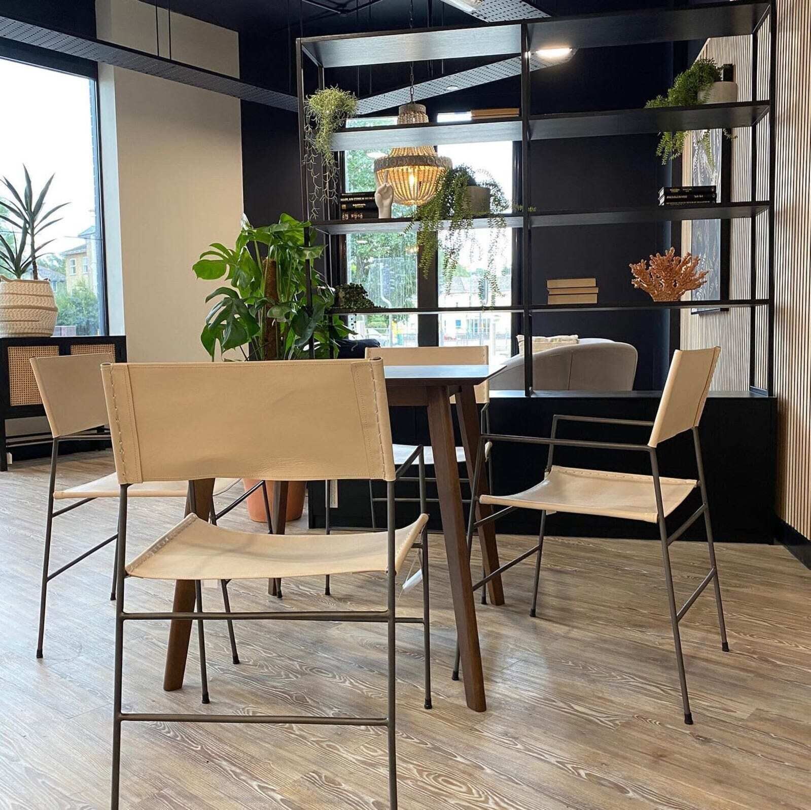 A modern interior with a wooden floor, a dining table with chairs, a sofa, and a bookshelf with decorative items.