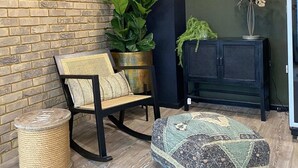 A room with a brick wall, a black sofa, a large potted plant, a small table with a decorative item, and a patterned ottoman. - Student Only Home Park (Bournemouth)