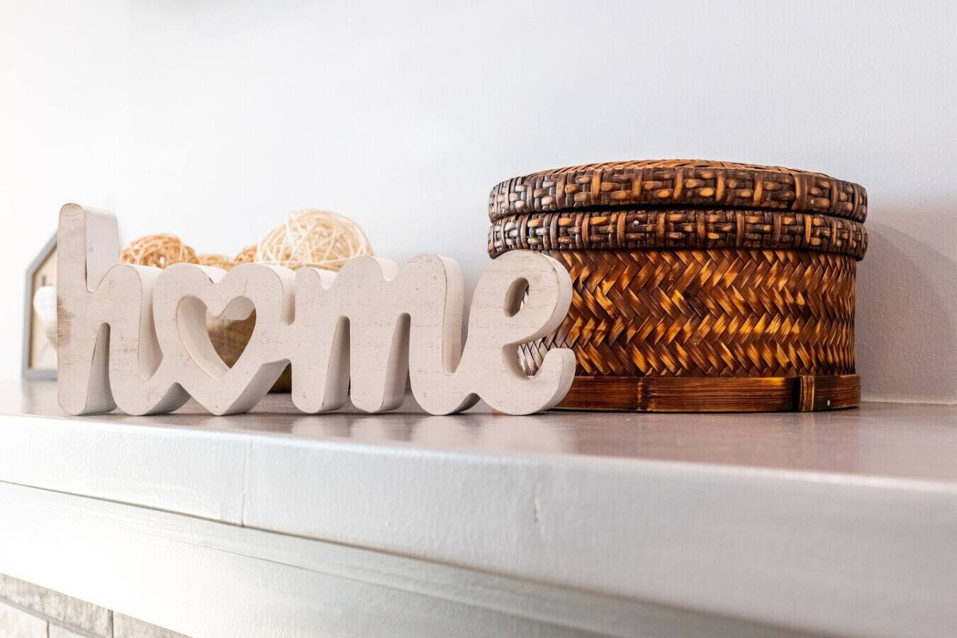 Un panier en osier orné d’un motif tissé et une plaque en bois sur laquelle est inscrit le mot « maison », le tout posé sur une surface blanche.