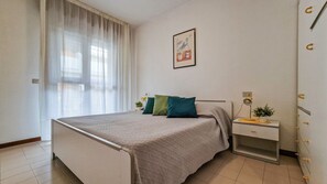 Una camera da letto con un letto, un comodino, una lampada e una finestra con tende.