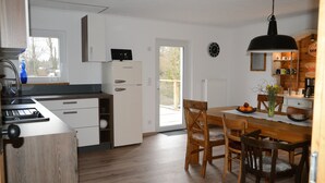 Una cocina moderna con armarios blancos, horno empotrado y comedor con sillas y mesa de madera.