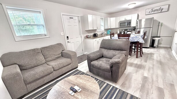A living room with a sofa, armchair, and coffee table, a kitchen with appliances, and a dining area.