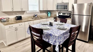 A compact kitchen with white cabinets, a stainless steel refrigerator, a microwave, and a dining table set with plates and glasses.