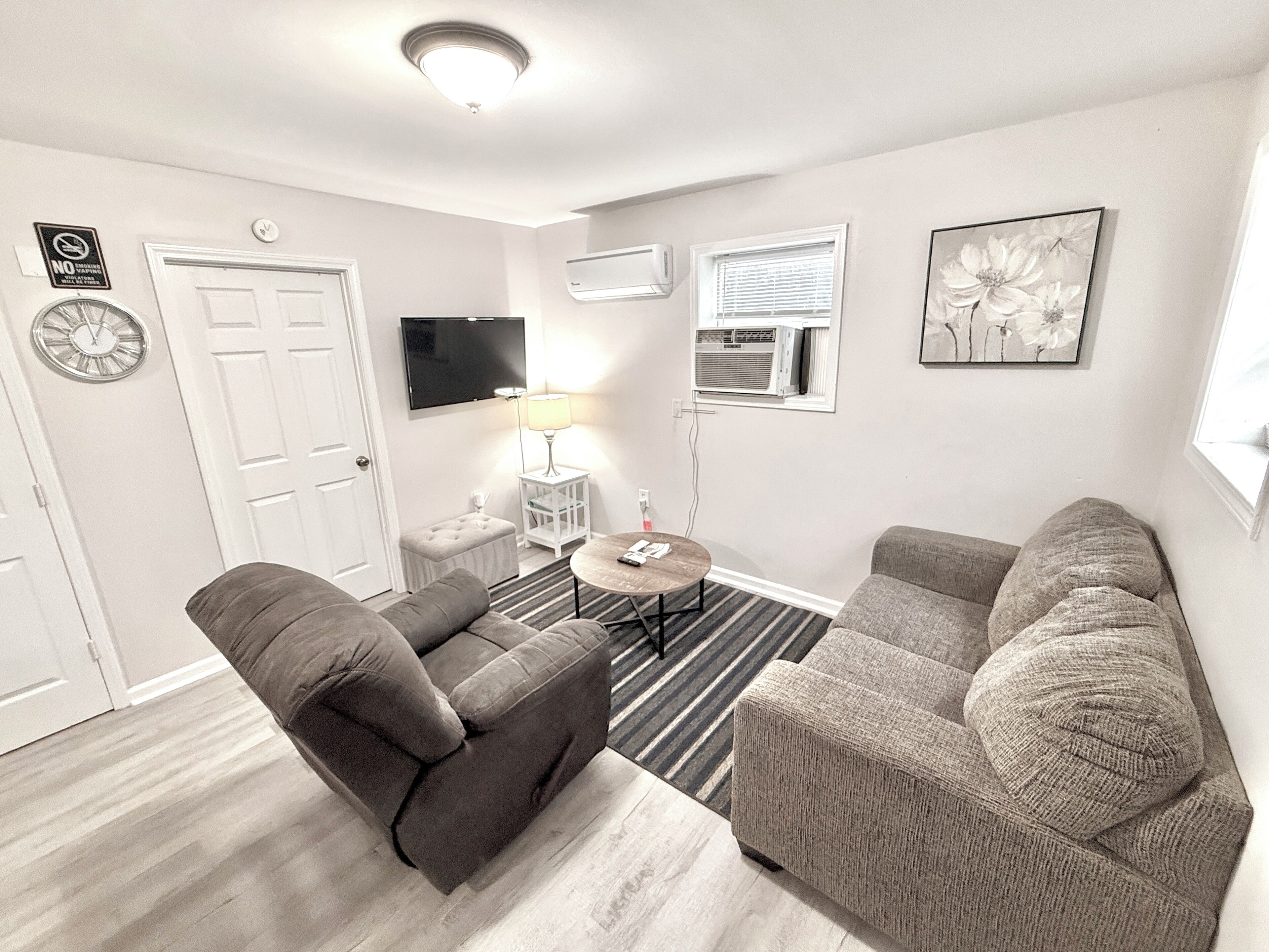 A modern living room with two sofas, a small round table, a TV, and a clock on the wall.