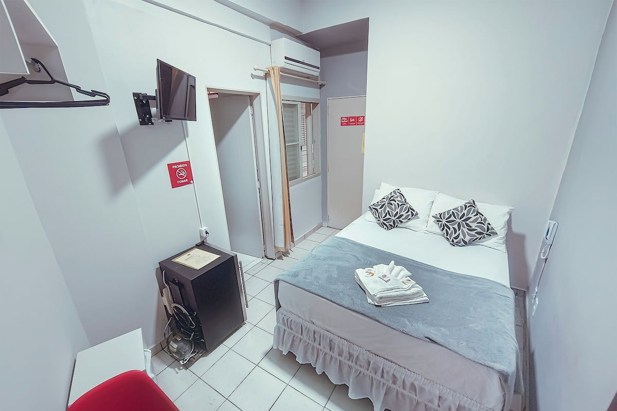 A small, compact bedroom with a bed, a TV mounted on the wall, and a red "No Smoking" sign.