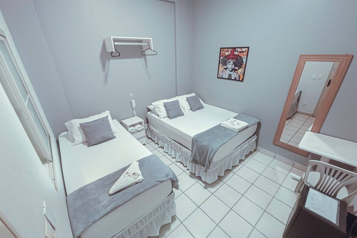 A bedroom with two beds, a bedside table with a lamp, a wall-mounted shelf, a mirror, and a poster on the wall.