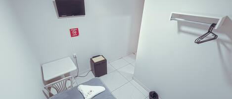 A small, clean room with a bed, a TV mounted on the wall, a small table, and a trash bin.