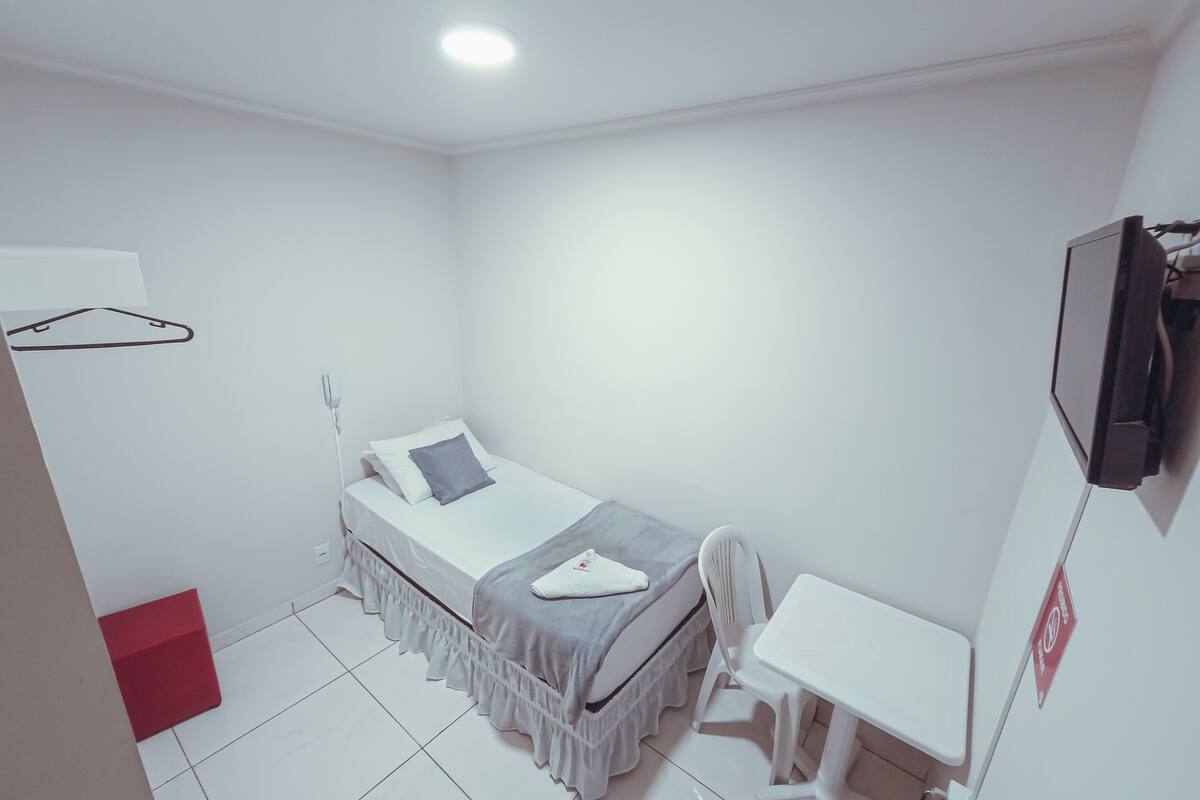 A small, white room with a single bed, a desk, and a chair.