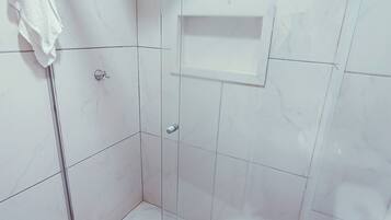 A modern bathroom with a glass-enclosed shower, a white toilet, and a small shelf.
