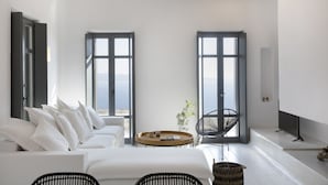 Ein modernes, minimalistisches Wohnzimmer mit einem weißen Sofa, zwei großen Fenstern, einem runden Couchtisch und einem schwarzen Sessel.