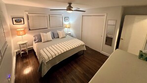 Quarto com cama, duas luminárias de cabeceira, ventilador de teto e uma porta.