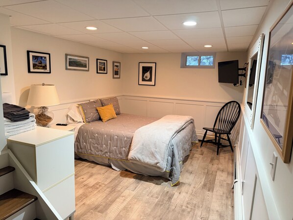 Une chambre à coucher avec un lit, une chaise, un bureau avec une lampe et des tableaux encadrés accrochés au mur.