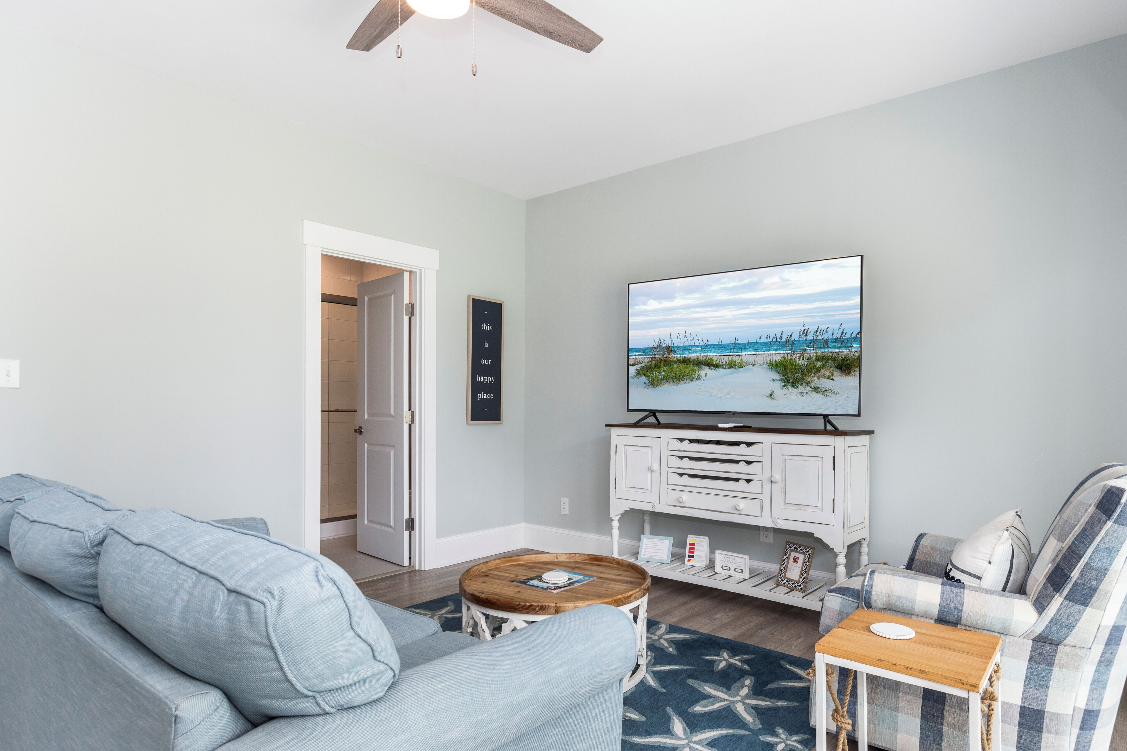 Una sala de estar con un sofá, una mesa de centro, un televisor sobre un mueble y una puerta que da a otra habitación.