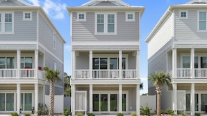 A two-story beachfront property with balconies, a covered entryway, and a small garden area.