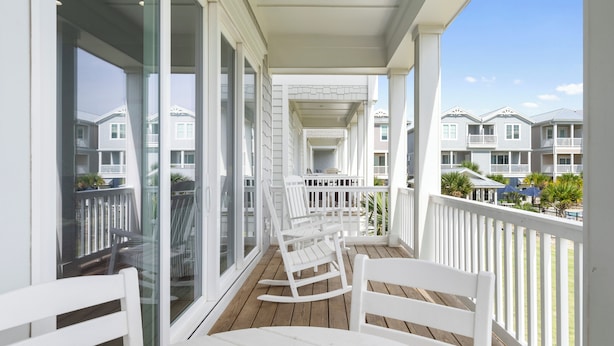 A balcony with white rocking chairs and a wooden floor, overlooking a row of townhouses.