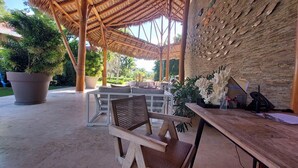 Un espacio al aire libre con estructuras de bambú, plantas en macetas y un muro de piedra con tallas de peces.