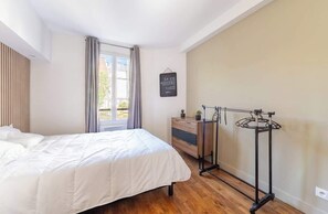 A bedroom with a bed, a dresser, a window with curtains, a wall-mounted sign, and a metal drying rack. - Parisian Flat for Work and Study (Paris)