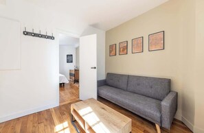 A modern living room with a grey sofa, wooden coffee table, and a wall with framed artwork. - Parisian Flat for Work and Study (Paris)