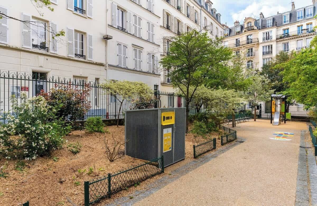 Ein Innenhof mit Umzäunung, einem kleinen Kiosk und einem Gebäude mit zahlreichen Fenstern und Balkonen.
