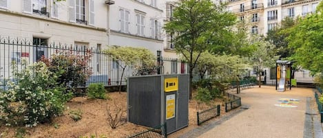 En innergård med ett inhägnat område, ett litet kiosk och en byggnad med flera fönster och balkonger.